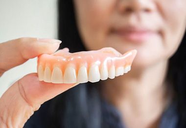 Woman holding upper denture in foreground of picture