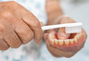 Hand of older person using soft brush to clean denture