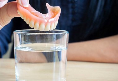 Person carefully placing denture in cup of water