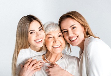 Older woman in white hugging two younger women in white smiling