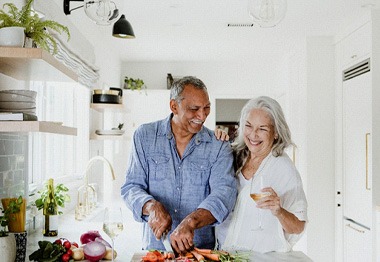 Man in blue shirt cooking with woman in white shirt while smiling